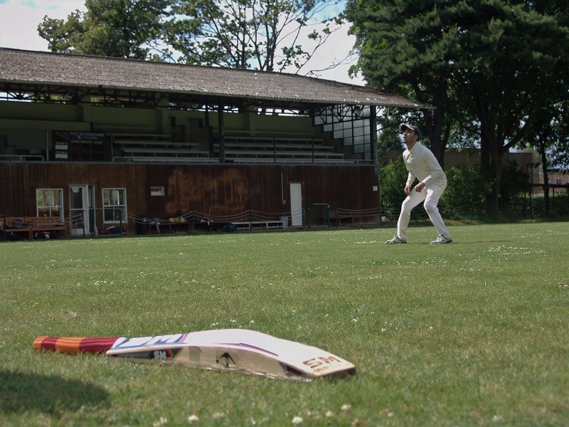 een jongeman wacht op een bal tijdens een crickettraining, de bat ligt op de voorgrond