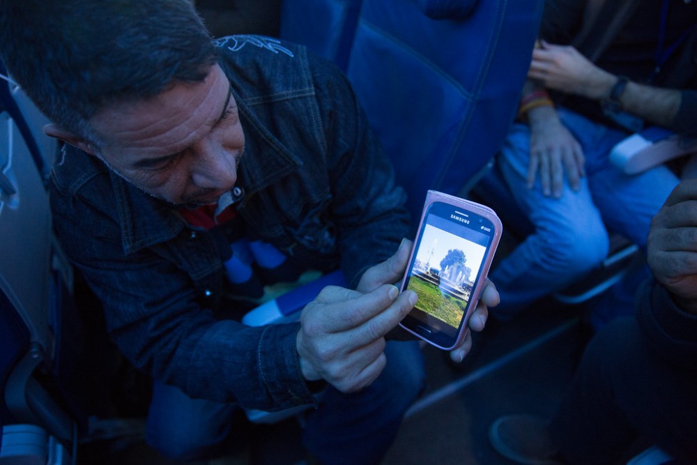 A Syrian refugee shows his home town of Hama on his phone while enroute to Canada. © IOM/Muse Mohammed 2015 (https://www.flickr.com/photos/iom-migration/24366713595)