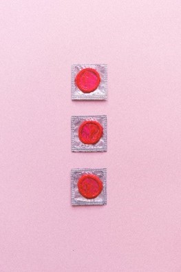 Drie roodkleurige condooms in hun verpakking