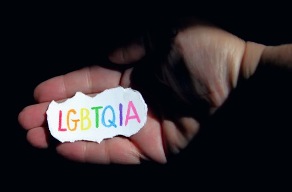 Een zwarte achtergrond met een hand waarin een papiertje waarop in regenboogletters LGBTQIA staat