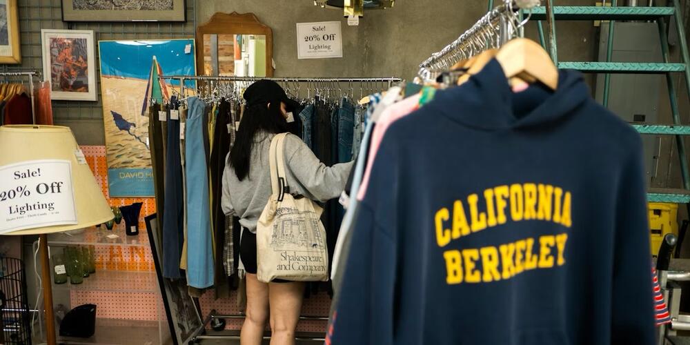 Een vrouw bekijkt kleding aan een rek in een vintagewinkel, met een donkerblauwe hoodie op de voorgrond.